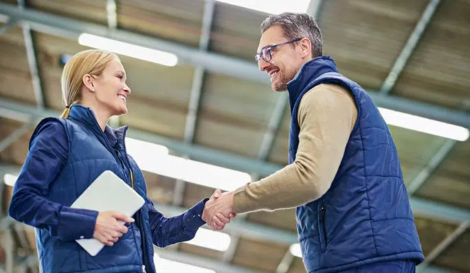Zwei Logistikexperten beim Beratungsgespräch und Handschlag in moderner Lagerhalle